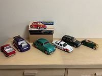 Front view of all six die-cast model cars displayed on wooden surface including Volkswagen Beetle in box and five other models.