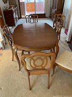 Dining table with four chairs arranged around it showing wood grain, shape, and chairs with upholstered seats.