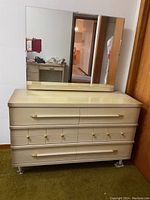 Front view of wooden dresser with attached mirror, showing gold-tone handles and knobs, and plastic wrappings on legs.