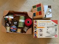 Overview of box with multiple spools of ribbon and trims, Dressmaker Sewing Center box, and Singer accessory box with sewing tools visible.