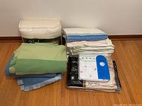 Image overview showing piles of folded green and blue wool blankets and various stacked sheets, some packaged.