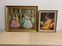 Two framed paintings on a wooden surface, featuring a ballroom dance scene and a young woman reading a book.