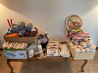 Wide shot showing all contents arranged on table including yarn, patterns, knitting needles, wool roving, and finished knitting project.