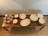 Full view of the china set laid out on a wooden table showing stacks of plates, cups, saucers, and two oval serving platters.