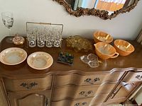 Full view of various glassware and ceramic bowls on a wooden dresser with mirror above