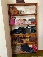 Front view of wooden shelving unit displaying various purses and handbags in different colors and styles across five shelves, plus one handbag on top of the shelving unit.