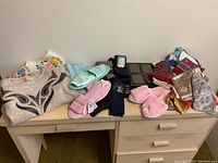 Entire lot showing all items including the sweaters, slippers, scarves, socks on top of a wooden dresser.