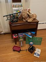 Photo of assorted toys on and in front of a small wooden cabinet including stuffed dog toy, blue biplane model, green stencil, red wagon, and other small items