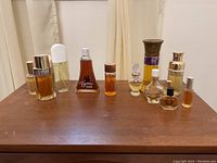 Front view of ten assorted perfume bottles placed on a wooden surface showing variety in size and style, with noticeable amber liquid in many bottles.