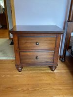 Front view of wooden side table showing two drawers with round knobs and turned feet.