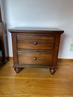 Front view of the wooden side table showing two drawers, round knobs, and bun feet.