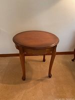 Full view of round wooden side table showing the tabletop surface and four curved legs.