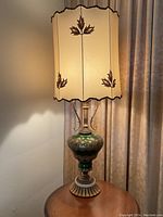 Full view of vintage decorative table lamp on wood table against curtain background.