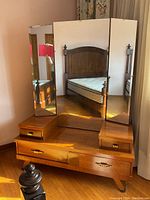 Front view of the vintage wooden dressing stand with tri-fold mirror reflecting a bedframe.
