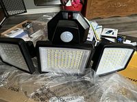 Front view of motion activated security light showing three LED panels and central motion sensor. Light is black with many small LED bulbs in rectangular panels.