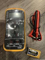 Photo of yellow digital multimeter with rotary dial and test leads. A 9V battery is placed beneath the multimeter.