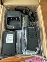 Opened box showing the Retevis two way radio, battery, charger dock, antenna, and power cord laid out in compartments.
