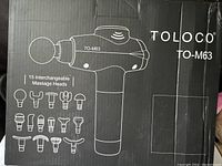 Box front showing image of black TOLOCO TO-M63 percussion massage gun with 15 illustrated interchangeable massage heads.