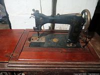 Side view of the Wheeler & Wilson #9 antique sewing machine showing black metal body with gold detailing mounted on wood table.