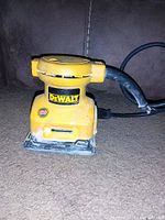 Yellow DeWalt 1/4 inch palm sander shown from side view, with visible wear and frayed power cord next to it