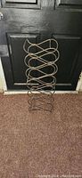 Photo of a metal wine rack standing upright on the floor in front of a door, showing the entire rack and its bottle holder structure.
