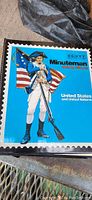 Photo of the cover of a Scott Minuteman stamp album featuring a colonial soldier in front of an American flag, indicating the time span and type of stamps included.