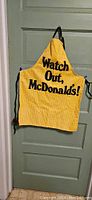 Photo of yellow apron with 'Watch Out, McDonalds!' text hanging on door.