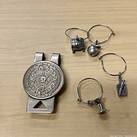 Top-down view showing the Aztec calendar money clip on left and four silver-tone hoop earrings with different charms on right.