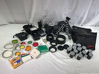 Full lot overview showing assorted camera filters in packaging, lens hoods, Vivitar flash, small black tripod, several empty film canisters and bags