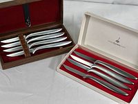 Photo showing set of four knives with polished blades and ergonomic silver handles in brown wooden box