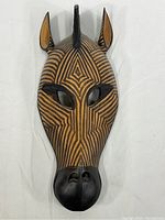 Front view of the finely carved and painted wooden animal mask from Kenya with geometric patterns and hollow eyes.
