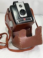 Kodak Brownie Hawkeye flash camera in brown leather case with front view showing lens, flash model plate and case strap.