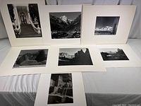 Overview of all seven mounted prints arranged on a white surface showing variety of landscape and architectural photography in black and white.