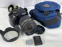 Overall view of Nikon D5100 with Tamron lens attached, lens hood, cap, battery, SD card and carrying pouch