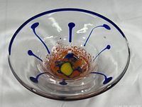 Top view of the signed hand blown art glass bowl showing clear glass with blue decorative highlights on the rim and orange and yellow abstract pattern in the center.