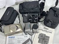Three cameras (Nikon CoolPix 4300, Olympus Stylus Epic Zoom 170, Panasonic Lumix DC-ZS70) with manuals and pouches