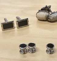 Five pairs of vintage silver tone cuff links displayed, showing variety of styles and black detailing.