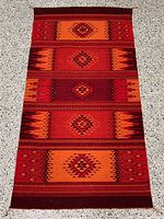 Full view of woven area rug with geometric patterns in sunset colors.