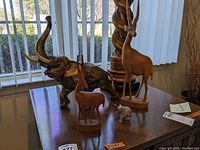 Group of four animal figurines on wooden surface: large textured nickel elephant, small white alabaster elephant, and two wooden gazelles, one tall and one medium height.