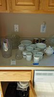 Overview of the lot showing sugar bowl, ramekins, coffee mugs, ceramic and glass bowls, and clear pitcher on a counter