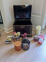 Open treasure chest style box with multiple assorted candles placed in front, showing various jar, votive, pillar, and tealight candles with different colors and designs.