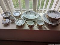 Wide view of entire china set with plates, bowls, cups, saucers, creamer, and sugar bowl displayed on window ledge.