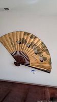 Full view of the large bamboo and painted paper decorative wall fan mounted on a wall, showing the folded ribs and artwork.