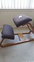 Side angle showing wooden frame and dark brown cloth upholstered seat and knee rest.