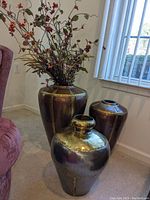 Three metal look planters/vases of varying sizes with hammered brass finish placed on floor near window and chair