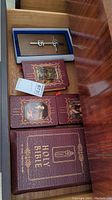 Top-down view of drawer showing four Moroccan leather covered Holy Bibles with gold embossing and a boxed metal cross on wood base.