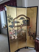 Front side of the room divider with golden background and Asian figures and landscape scenes.
