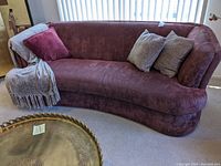 Front angle view of curved purple sofa with three pillows and beige throw draped on left armrest