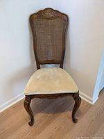 Full front view of Stanley chair with caned back and beige upholstery seat, showing wood frame and carved legs.