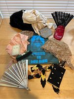 Photo showing assortment of hats, scarves, fans, bags, ceramic shoe planter, and other accessories arranged on a table.